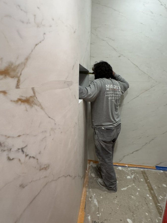 A Markell installer setting a full-slab porcelain shower wall